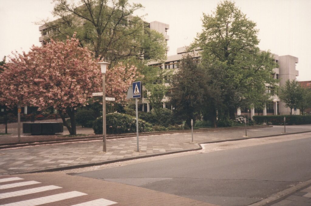 91er Strasse, Finanzamt, 1987, © Stadtmuseum Oldenburg Finanzamt-Gebäude an der 91er Straße in Oldenburg, umgeben von Bäumen mit Frühlingsblüten, aufgenommen 1987, © Stadtmuseum Oldenburg