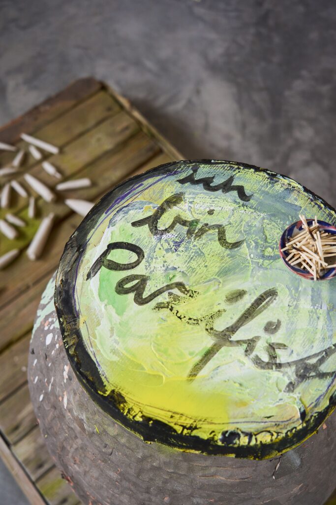 Carlo Leopold Broschewitz, Pulverfass V, Keramik, Holz, Streichhölzer, Acrylfarbe Buntstift, 2025, © Carlo Leopold Broschewitz Keramisches Pulverfass mit gelb-grün bemalter Oberfläche und schwarzer Schrift "ich bin Pazifist", darauf Schale mit benutzten Streichhölzern