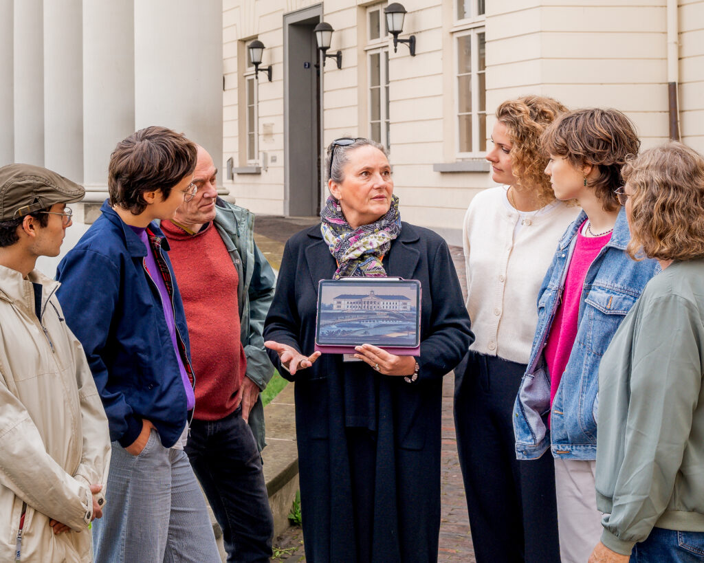 Eine Person hält ein Tablet mit historischem Bild des PFLs, umgeben von weiteren Personen im Bereich des PFLs, © Studio 3x3