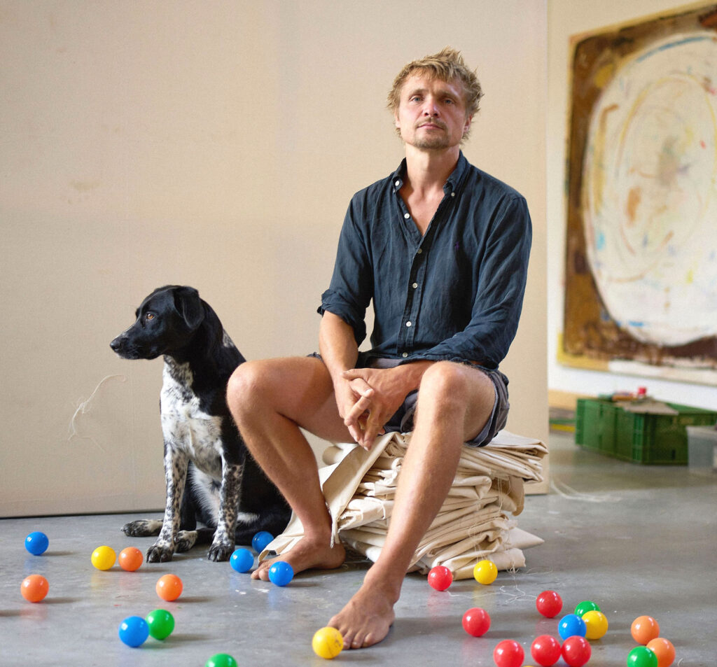 Porträt Carlo Leopold Broschewitz, © Tom Dachs Porträt von Carlo Leopold Broschewitz und Hund auf einem Stoffstapel sitzend mit bunten Bällen auf dem Boden, © Tom Dachs
