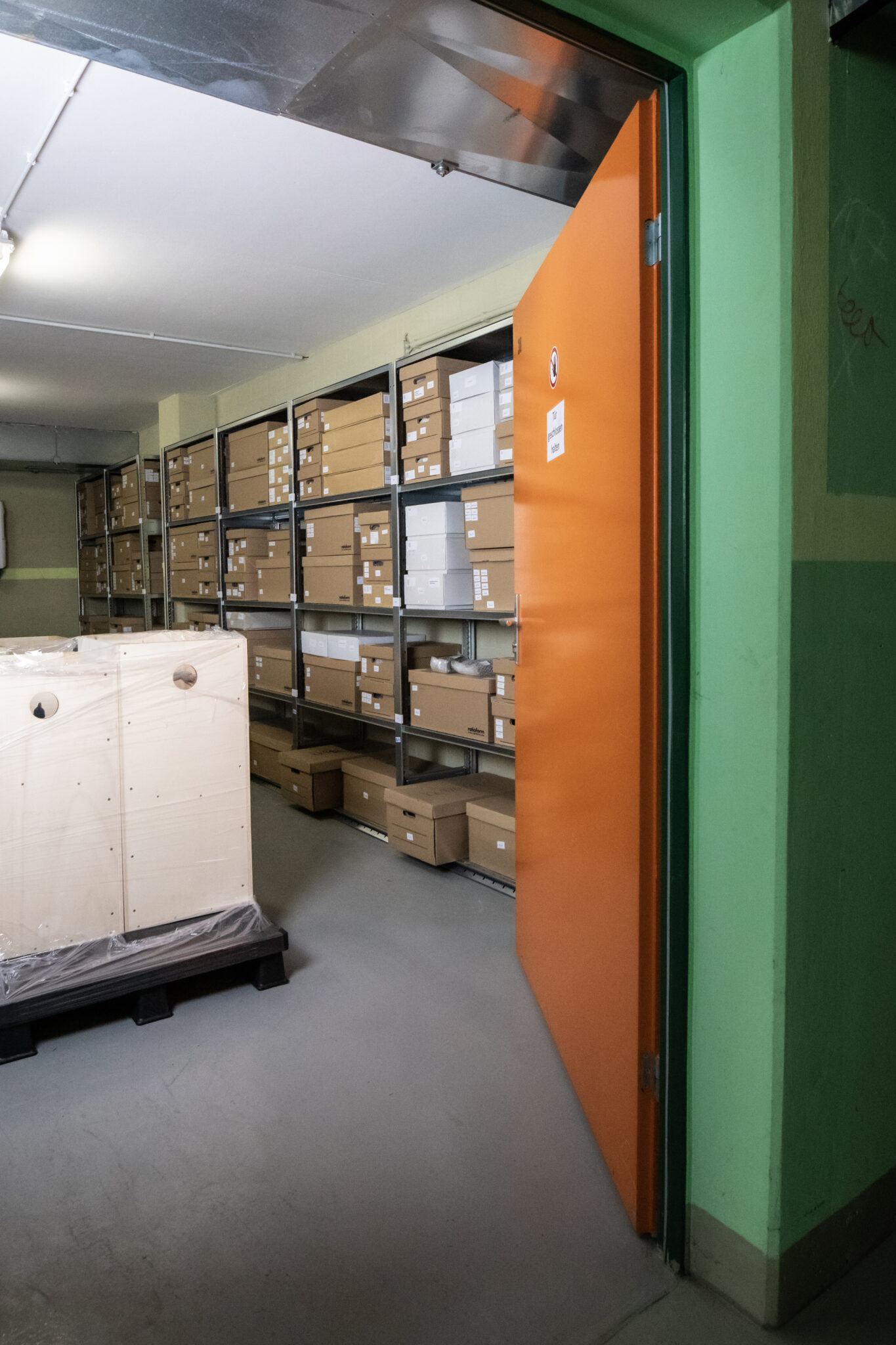 396A2665 Kopie Sicht in einen Lagerraum im Depot, darin Metallregale mit gestapelten Papierkisten und in der Mitte des Raums Holzkisten mit großen Kunstobjekten, © Gerlinde Domininghaus