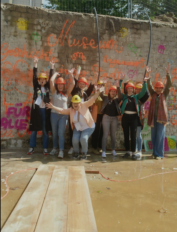 Gruppe von Personen jubelt vor einer Mauer mit orangenen Handschriften bei der Grundsteinlegung des neuen Stadtmuseums, © Stadtmuseum Oldenburg