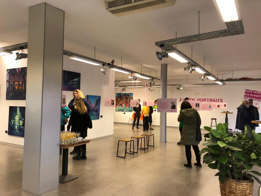 Ausstellungsraum der Re:Claim-Ausstellung mit Menschen, Sitzgelegenheiten und Bildern an den Wänden, © Re:claim Oldenburg