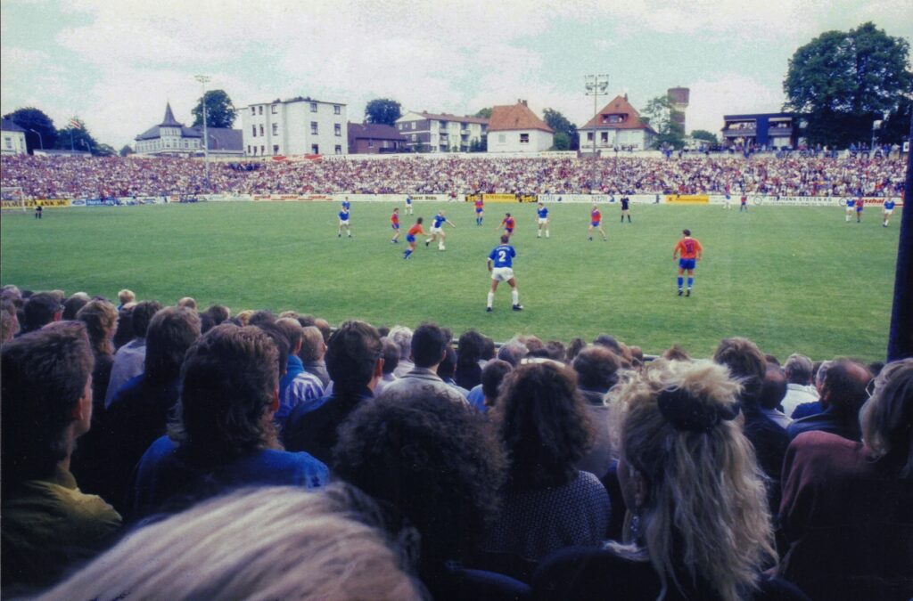 BA 22219 Peter Kreier VfB Stadion Blick Auf Wasserturm 1990 Fußballspiel im VfB Stadion 1990, Zuschauer im Vordergrund, Spieler auf dem Spielfeld, Wasserturm und Wohnhäuser im Hintergrund, © Peter Kreier