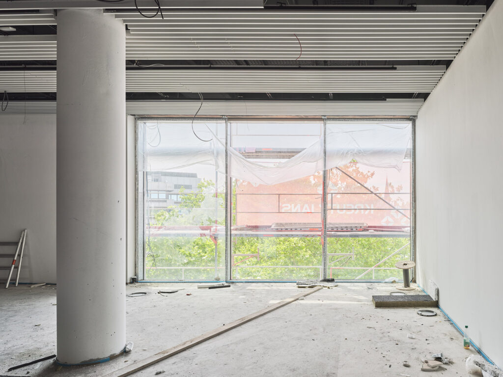 Blick auf ein Fenster auf der Baustelle mit Betonboden und unvollständiger Decke, © Caspar Sessler