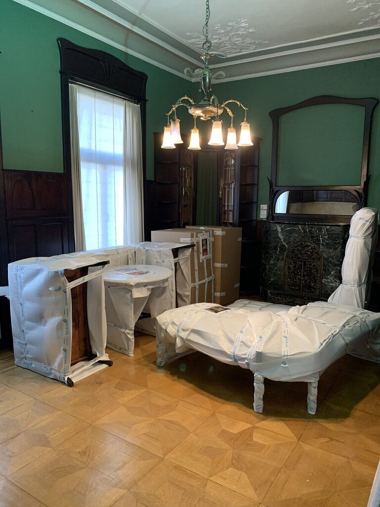 Herrschaftliches Arbeitszimmer mit grünen Wänden, Kronleuchter und eingepackten Möbelstücken auf dem Parkettboden, © Stadtmuseum Oldenburg