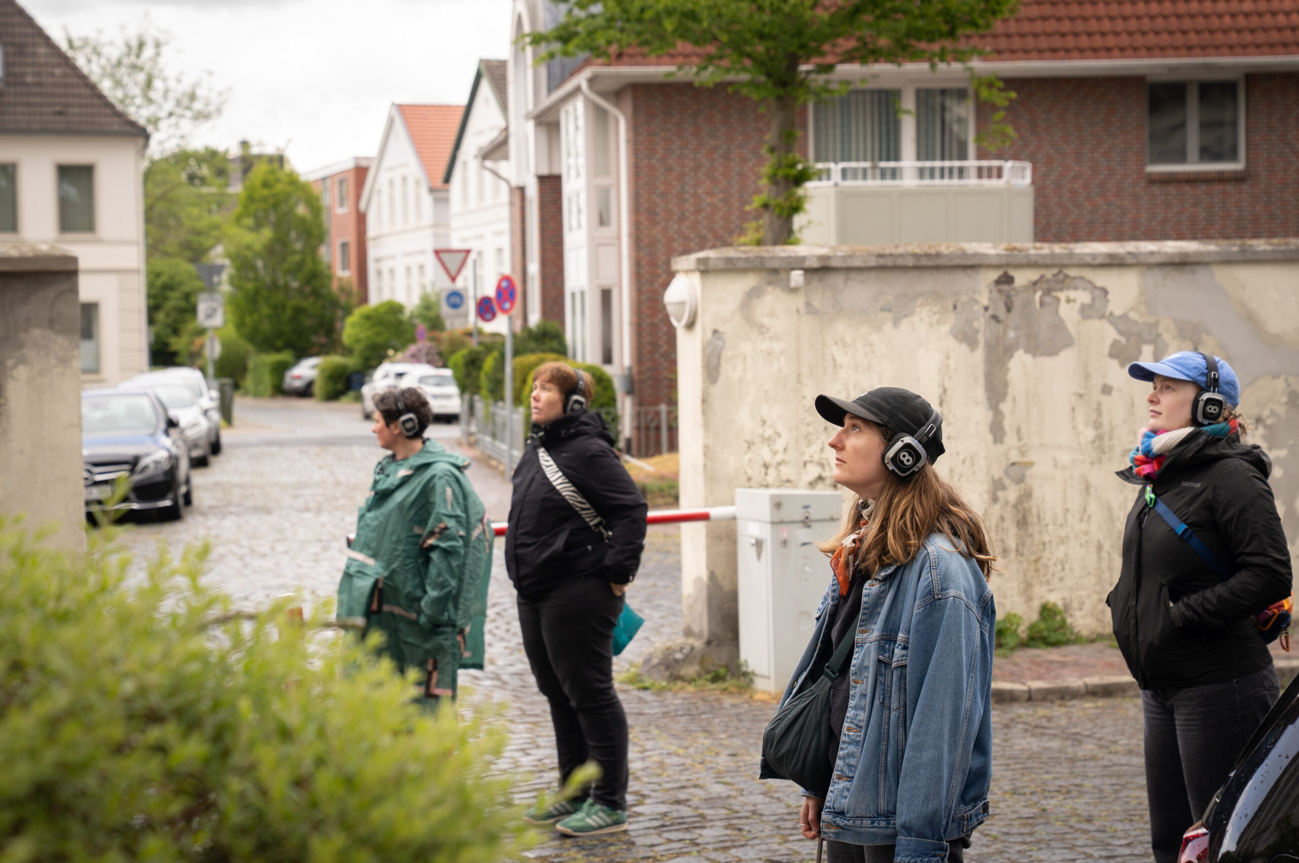 Personen mit Headsets stehen auf einem Platz mit Kopfsteinpflaster, schauen in eine Richtung, im Hintergrund Wohnhäuser, © Stephan Walzl