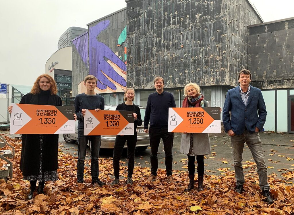 Sechs Menschen stehen auf herbstlich bedecktem Boden vor der Neuen Galerie, vier von ihnen insgesamt drei Spendenchecks in den Händen, © Stadtmuseum Oldenburg