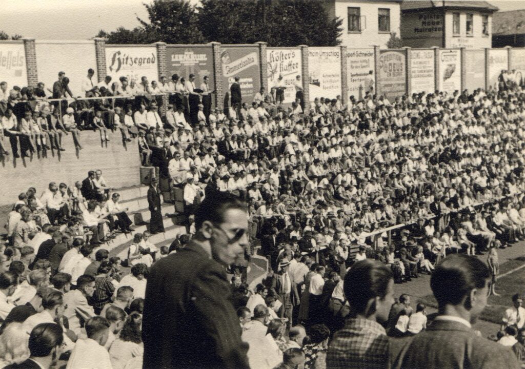 Stadion Donnerschwee V 3 Nr. 3,Platzeinweihung 1948 Große Menschenmenge auf Tribüne bei Platzeinweihung im Stadion Donnerschwee 1948, viele sitzen und stehen, Werbetafeln im Hintergrund, © Stadtmuseum Oldenburg