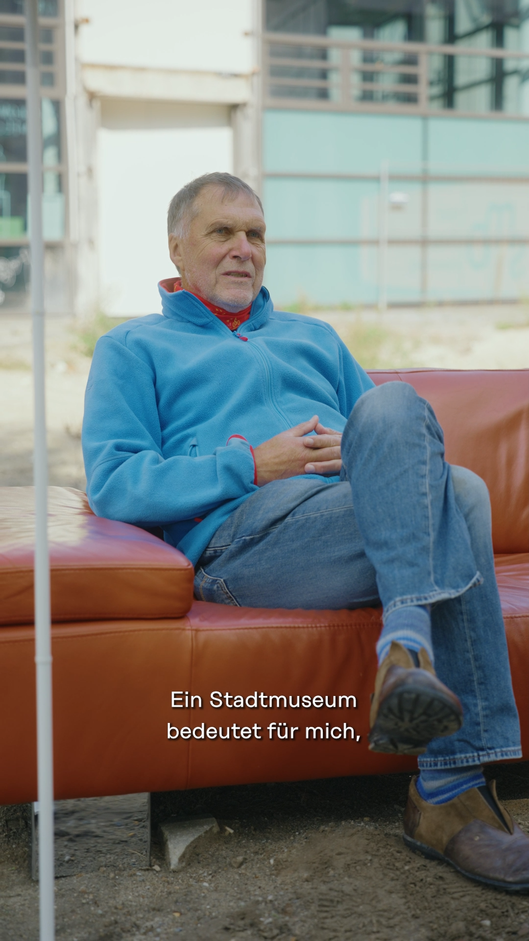 Ältere Person sitzt zurückgelehnt auf rotorangenem Sofa, im Hintergrund das Horst-Janssen-Museum, © Stadtmuseum Oldenburg