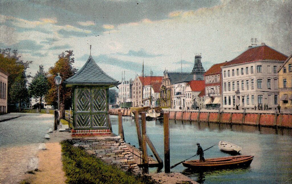 Malerei eines Gewässers mit Befestigung im Rand, im Vordergrund ein kleiner Unterstand aus Holz, über das Wasser fährt ein kleines Boot mit einem Menschen, © Stadtmuseum Oldenburg