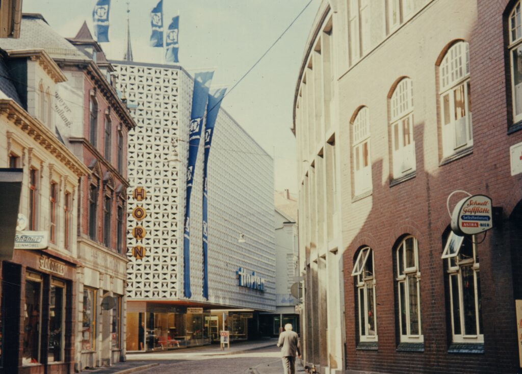 Blick die Straße hinunter auf ein Gebäude mit gekachelter Fassade und blauen Flaggen, © Stadtmuseum Oldenburg/Sammlung Schäfer