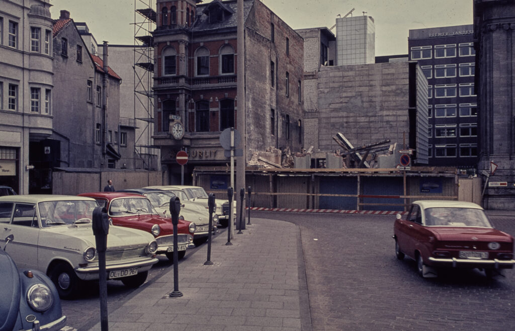 Autos stehen auf einem Parkplatz mit Parkuhren, im Hintergrund eine Baustelle, © Stadtmuseum Oldenburg/Sammlung Willy Schröder