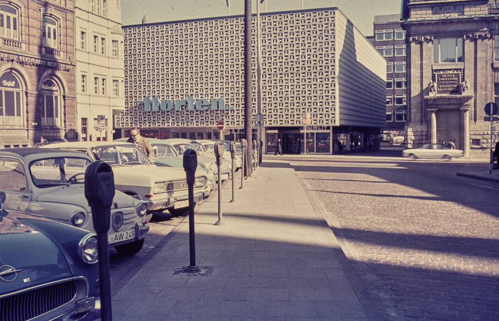 Autos stehen auf einem Parkplatz, im Hintergrund gGebäude, darunter ein Kaufhaus mit gekachelter Fassade und Aufschrift "Horten", © Stadtmuseum Oldenburg/Sammlung Willy Schröder