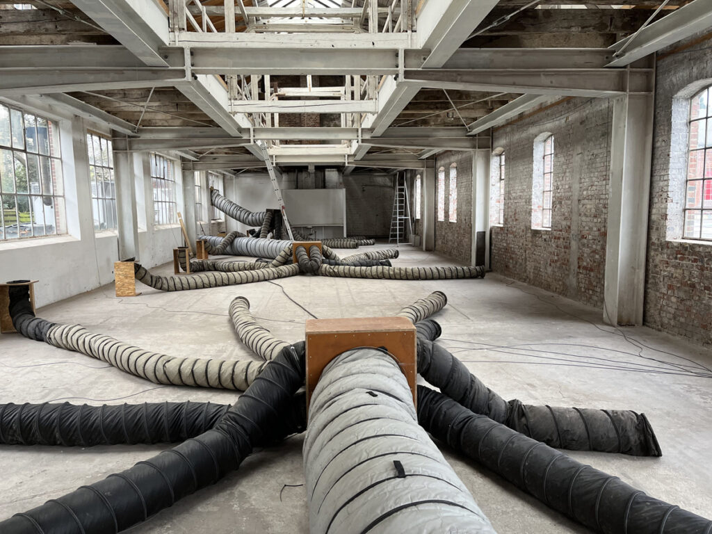 Sanierung der alten Maschinenhalle, 2024, © Stadt Oldenburg Große Schläuche liegen in einer leeren Halle mit Backsteinwänden, © Stadt Oldenburg