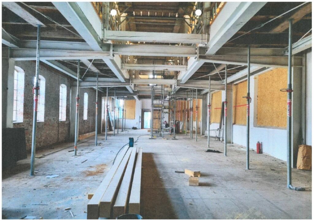 Innenansicht der Baustelle in der alten Maschinenhalle, 2024, © Katharina Semling Halle mit Baugerüsten, in der Mitte liegen Holzbalken, © Katharina Semling