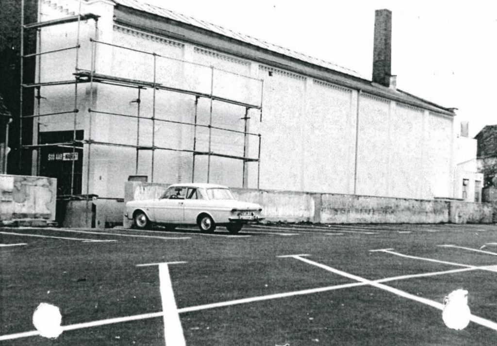 Die Halle mit dem neu entstandenen Parkplatz, 1967, © Urheber unbekannt Ein Auto steht auf einem Parkplatz vor einer hellen Wand mit Baugerüst, © Urheber unbekannt