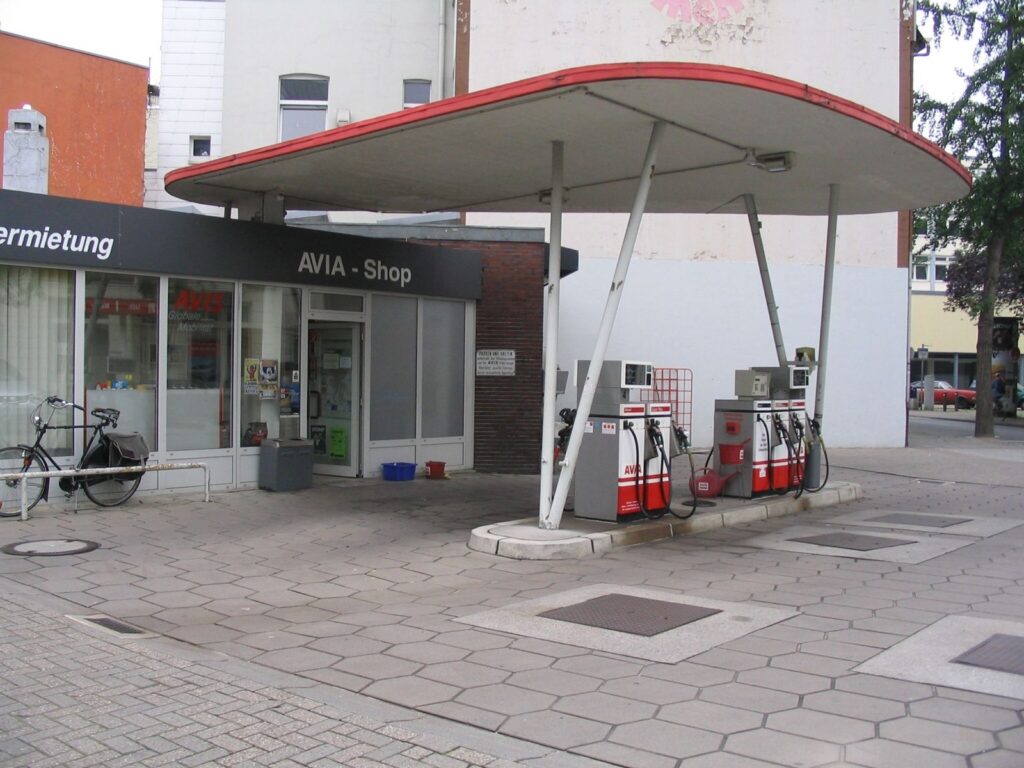 Vordach einer Tankstelle, darunter Zapfsäulen, im Hintergrund Tankstellengebäude