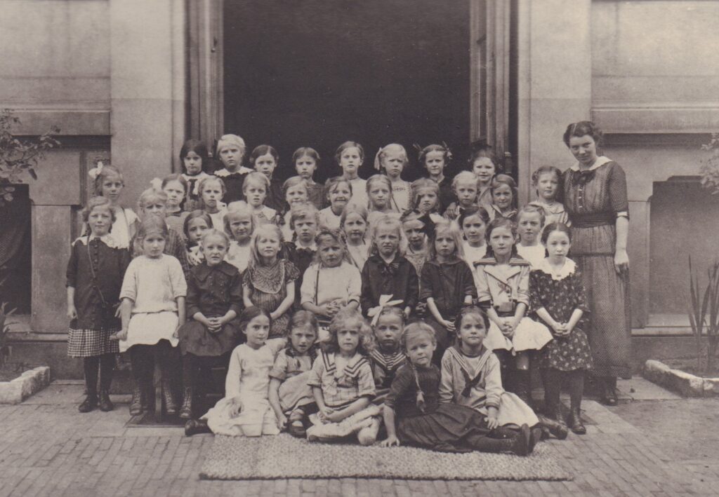 Klassenfoto mit vielen Kindern und einer Frau vor einem Hauseingang, © Stadtmuseum Oldenburg/Slg. Friederichsen