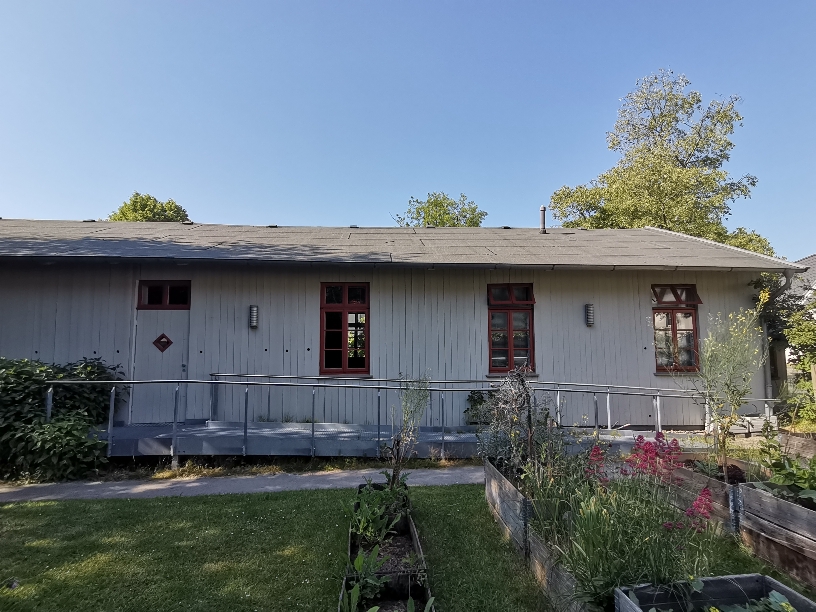 Flacher Bau mit Holzverkleidung und Rampe zur Tür, davor ein Garten, © Privat/Stadtmuseum Oldenburg.