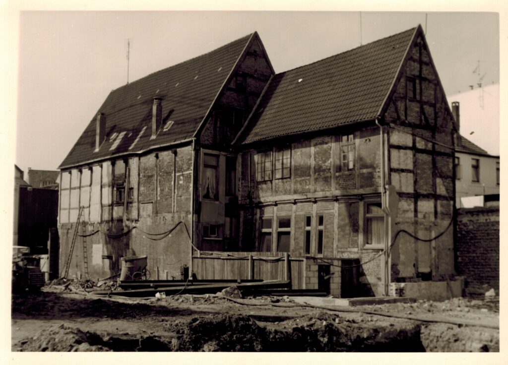Abb. 4 Zwei aneinander gebaute Fachwerkhäuser. davor eine Bauchstelle mit Werkzeugen, © Stadtmuseum Oldenburg, Slg. Günter Müller