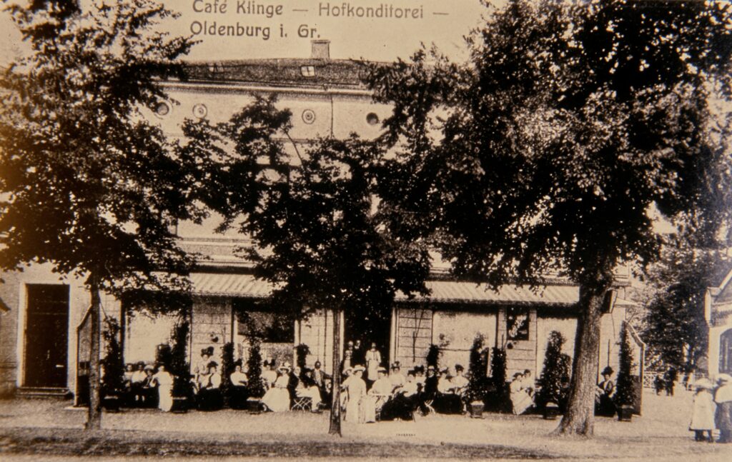 Abb. 5 Café Klinge Um 1900 Ein weißes Gebäude hinter Bäumen, davor sitzen Menschen, © Stadtmuseum Oldenburg, Slg. Willy Schröder