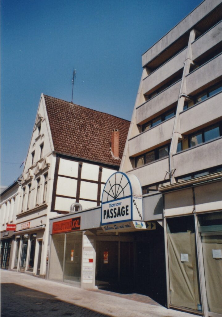 Abb. 6 Weißes Fachwerkhaus eingebaut in eine Häuserzeile, im Vordergrund Eingang in eine Passage, darüber ein Schild, © Friedrich Precht