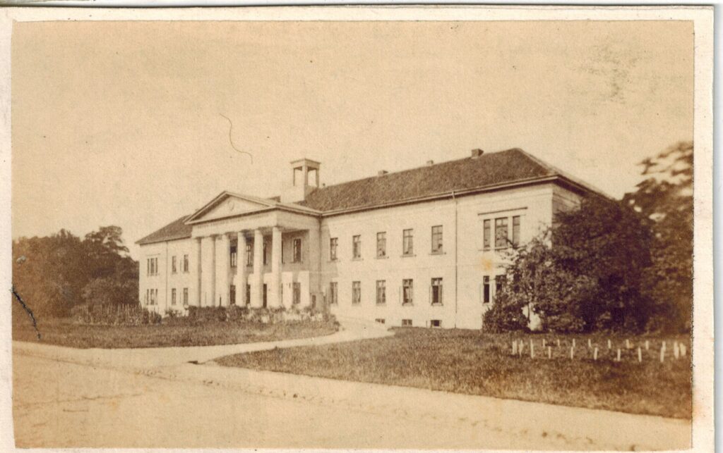 Abb. 8 BA 15535 Peter Friedrich Ludwig Hospital 1860 Historische Fotografie des Hospitals, weißer Bau mit Säulen, davor Grünfläche und eine Straße, © Stadtmuseum Oldenburg