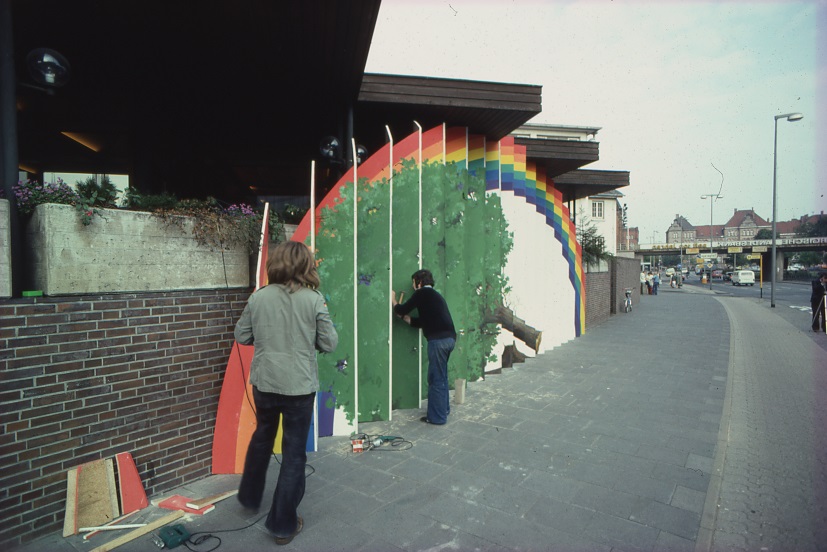 Abb.1 Zwei Personen arbeiten an einem Kunstwerk an einer Mauer, rechts ein Bürgersteig und Straße, © Stadtmuseum Oldenburg/Gerresheim