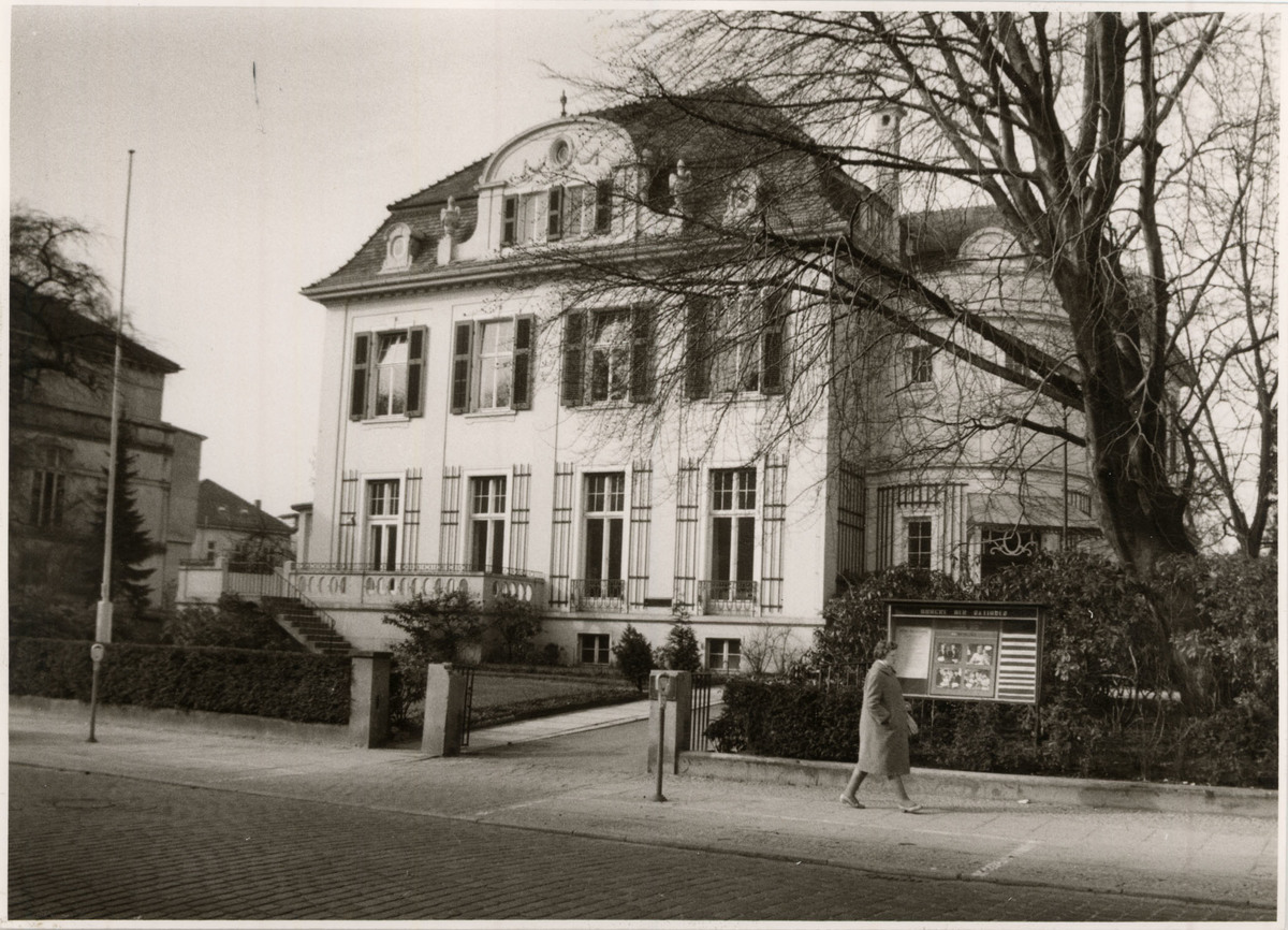 Die Nummer 5 – das für manch eine:n schönste Haus der Gartenstraße, 1978, © Stadtmuseum Oldenburg Weißes mehrstöckiges Gebäude mit vielen Fenstern hinter einem Zaun, eine Person geht die Straße entlang, © Stadtmuseum Oldenburg