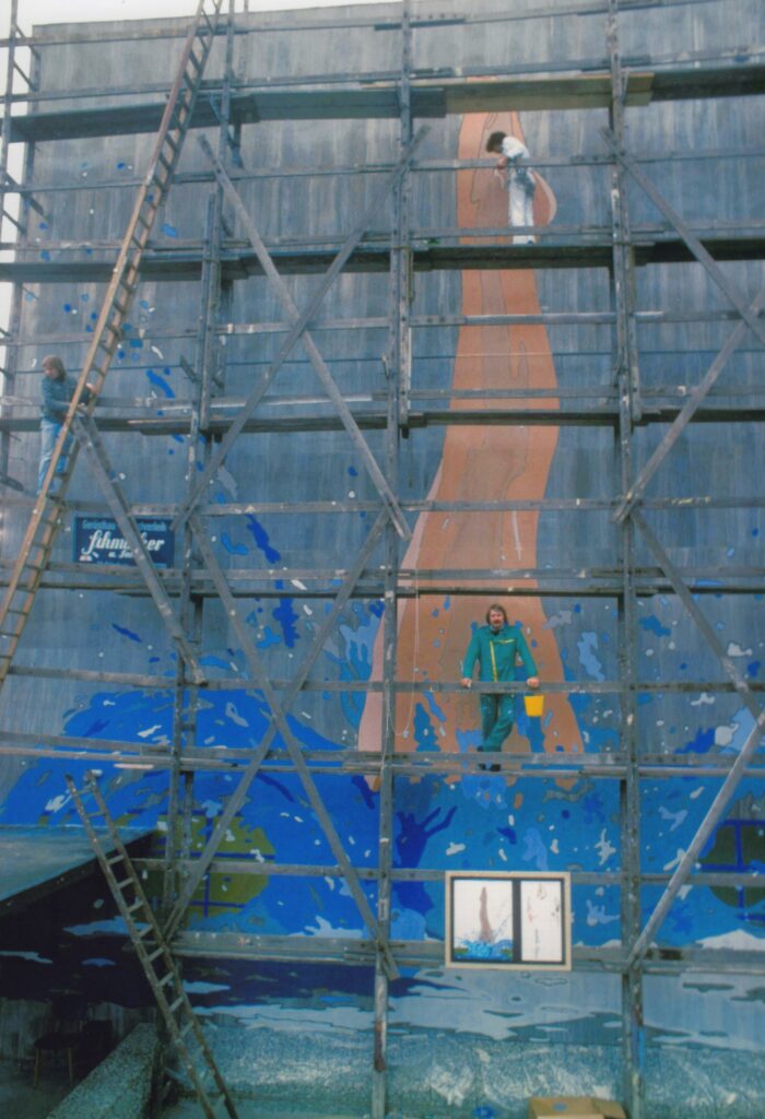 Abb.2 Abstrakte Malerei eines Menschen, der ins Wasser springt, blaues Wasser spritzt auf, vor der Wand ein Gerüst und zwei Personen, © Peter Kreier/Stadtmuseum Oldenburg