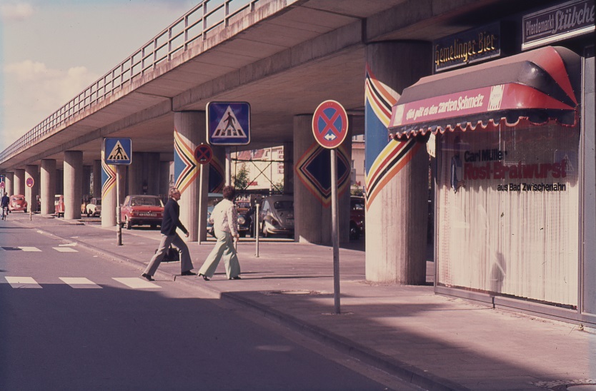 Abb.4 Säulen der Bahnbrücke, bemalt mit bunter Farbe, Menschen laufen auf der Straße, © Stadtmuseum Oldenburg