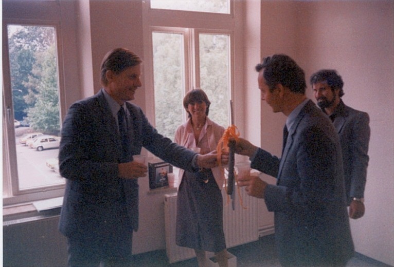 Vier Personen in einem weiß gestrichenen Raum, einer überreicht dem anderen ein Geschenk, © Artothek Oldenburg