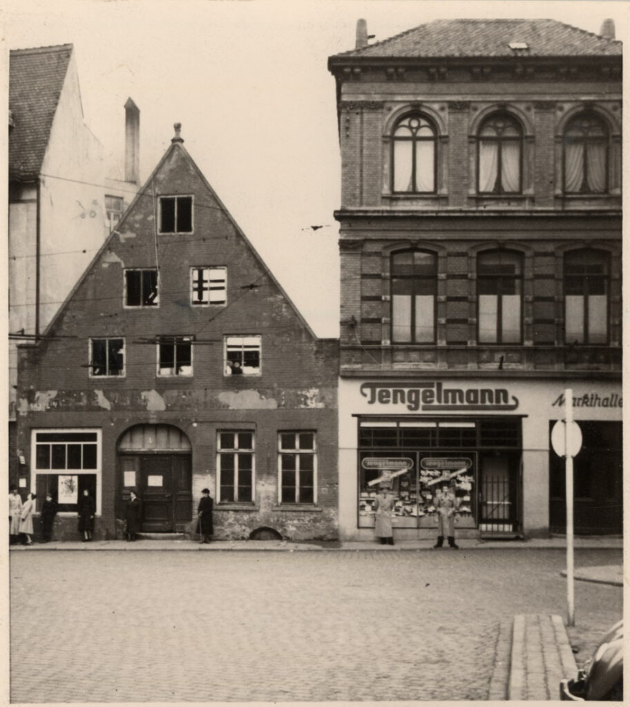 Ansicht zweier Gebäude, links, Backsteinfassade mit starken Schäden, rechts, ein Geschäft mit großem Schaufenster, © Stadtmuseum Oldenburg
