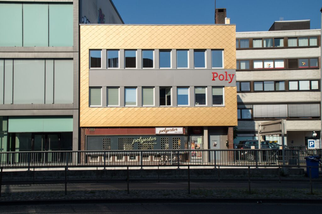 Poly-Haus mit neuer Fassade von 2016, dreistöckiges Gebäude mit gelblicher Verkleidung und Schriftzug 'Poly' an der Fassade, © Polygenos Kulturräume eG