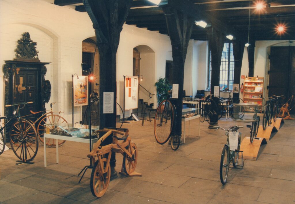 Ein Blick in die Dauerausstellung des Oldenburger Fahrradmuseums, © Stadtmuseum Oldenburg/Prov. Kalle Kalkhoff Halle mit dunklen Holzbalken und Holzsäulen, dazwischen stehen verschiedene Arten von Fahrrädern, © Stadtmuseum Oldenburg/Prov. Kalle Kalkhoff