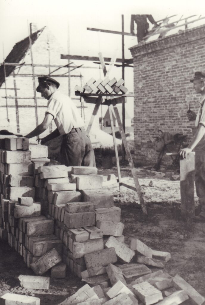 Gestapelte Backsteine auf einer Baustelle, im Hintergrund eine Backsteinmauer und Baugerüste aus Holz, einige Männer arbeiten, © GSG Oldenburg