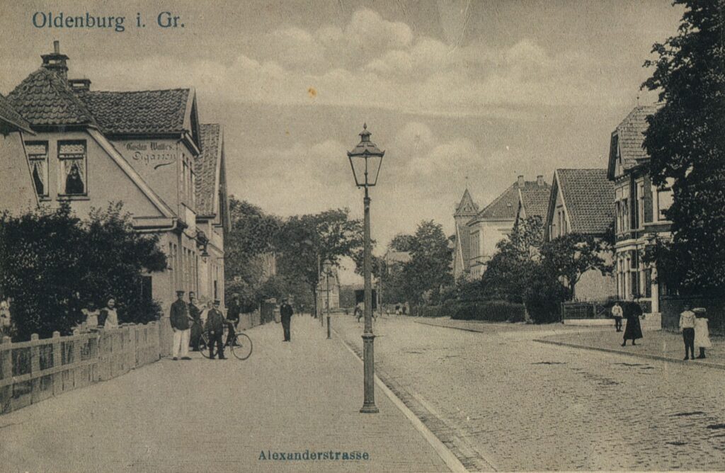 Straßenansicht mit Kopfsteinpflaster, Häuserzeilen, einige Personen stehen am Straßenrand, © Stadtmuseum Oldenburg