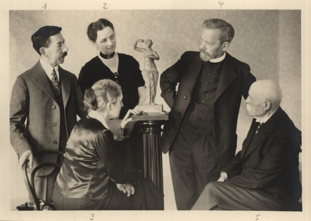 Mehrere Personen stehen um eine kleine Statue auf einem Sockel herum und betrachten sie, zwei Personen sitzen, © Stadtmuseum Oldenburg