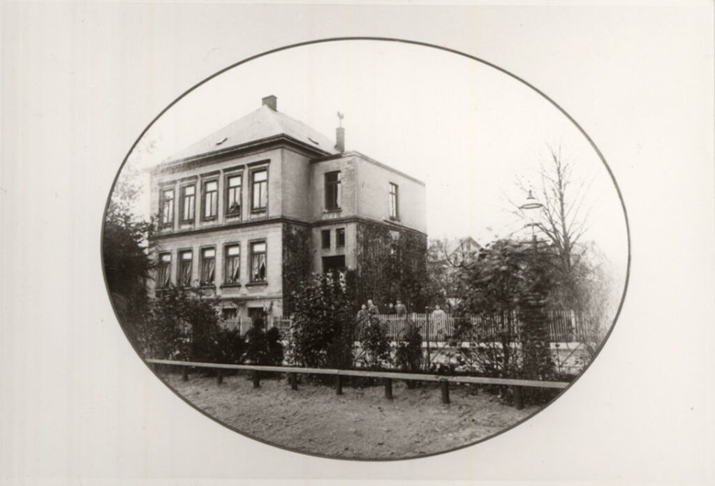 Im Vordergrund Büsche, dahinter ein mehrstöckiges Haus mit vielen Fenstern, im Garten daneben einige Personen, © Stadtmuseum Oldenburg