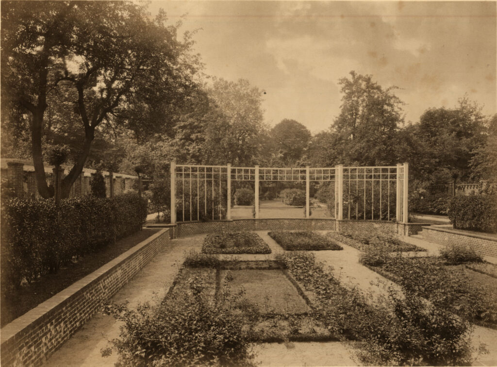 Historische Ansicht eines Gartens mit Beeten, umgeben von Bäumen, links eine niedrige Backsteinmauer, © Stadtmuseum Oldenburg
