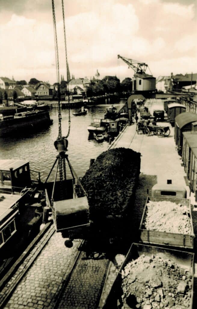 Mehrere Kräne waren am Stadthafen im Einsatz, darunter auch Halbportalkräne. Diese laufen über eine Schiene am Boden und eine Schiene an einer Mauer oder Brücke, 1950er Jahre, © Stadtmuseum Oldenburg